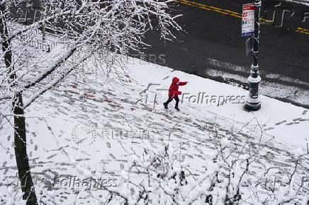 A child runs along a sidewalk holding a snowball during the city's first snowfall of the season, on the first day of winter in the Queens borough of New York City