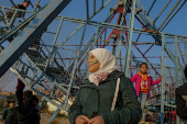 A girl with her face painted with the flag adopted by the new Syrian rulers stands as children play on a swing boat at an amusement park, in Douma