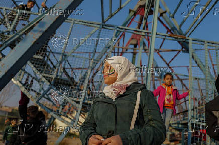 A girl with her face painted with the flag adopted by the new Syrian rulers stands as children play on a swing boat at an amusement park, in Douma