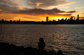 The sun sets behind the Lower Manhattan skyline in the Brooklyn borough of New York City