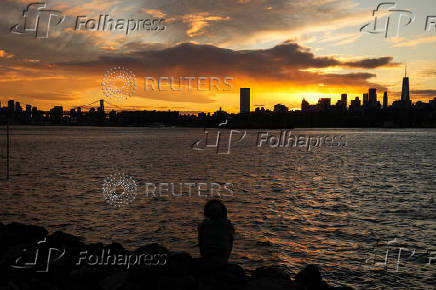 The sun sets behind the Lower Manhattan skyline in the Brooklyn borough of New York City