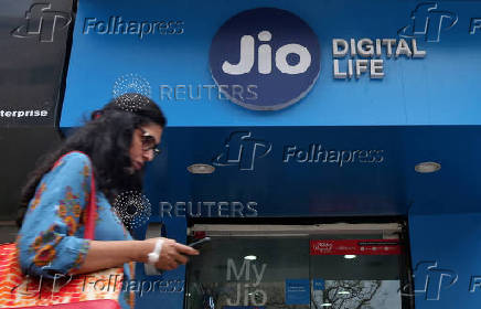 FILE PHOTO: A woman checks her mobile phone as she walks past a mobile store of Reliance Industries' Jio telecoms unit in Mumbai