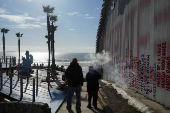 People walk by the Mexico-U.S. border fence at Playas Tijuana