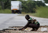 FILE PHOTO: A woman gathers grain spilled by cargo trucks from Zambia along a highway in Magunje