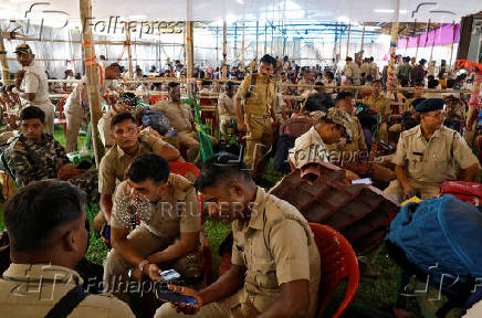 Police officers use their phones as they wait to be deployed on election duties at a distribution centre in Alipurduar