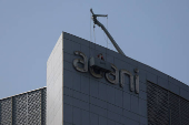 Men fix the logo of the Adani Group on the facade of its Corporate House on the outskirts of Ahmedabad