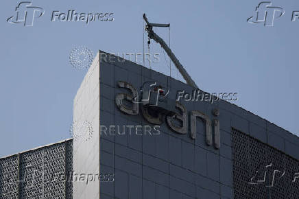 Men fix the logo of the Adani Group on the facade of its Corporate House on the outskirts of Ahmedabad