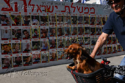 A man and a dog ride past posters with pictures of hostages kidnapped in the October 7 attack by Hamas, in Tel Aviv