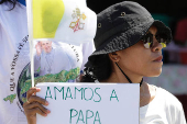 A woman holds a paper and a flag as she welcomes Pope Francis, before his arrival in Dili