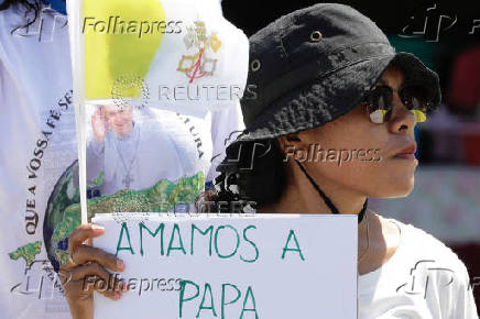 A woman holds a paper and a flag as she welcomes Pope Francis, before his arrival in Dili