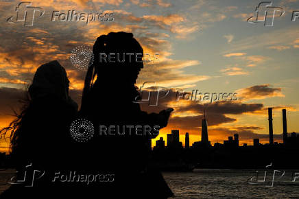 The sun sets behind the Lower Manhattan skyline in the Brooklyn borough of New York City