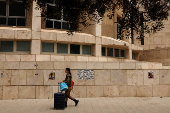 A woman dressed in military clothes walks past posters with pictures of hostages in Tel Aviv