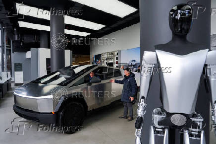 A Tesla Bot stands on display as people look at a Tesla Cybertruck at a Tesla showroom in New York City