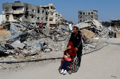 A Palestinian man pushes a child on a wheelchair amidst the rubble of buildings destroyed during the Israeli offensive, amid a ceasefire between Israel and Hamas, in Rafah