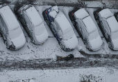 A worker cleans a street where cars are covered in snow amid the first snowfall in Kyiv