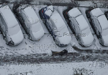 A worker cleans a street where cars are covered in snow amid the first snowfall in Kyiv