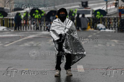 A man covers himself in a thermal blanket as he takes part in a protest against the impeached South Korean President Yoon Suk Yeol near his official residence on a snowy day in Seoul