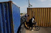 Men move a motorcycle amid shipping containers, used to block the area for security measures, following the visit of the Iranian President Ebrahim Raisi, in Karachi