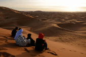 People sit at the top of a dune at the Erg Chebbi sand dunes in the Sahara desert outside Merzouga