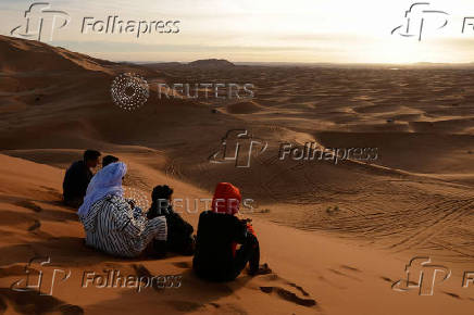 People sit at the top of a dune at the Erg Chebbi sand dunes in the Sahara desert outside Merzouga