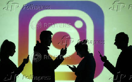 FILE PHOTO: Silhouettes of mobile users are seen next to a screen projection of Instagram logo in this picture illustration