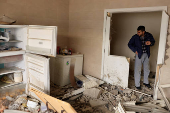 A man smokes a cigarette as he stands inside his destroyed home in the city of Baalbek,