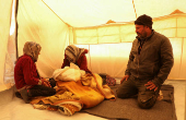 Displaced Syrian-Yazidi man Mohamed Nassro and his wife Shafiqa Saeeda, who fled from the Aleppo countryside sit together inside a tent next to their grandchild in Tabqa