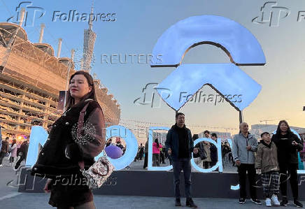 People pose for pictures in front of a sign of Nio at the electric vehicle (EV) maker's annual event NIO Day in Guangzhou