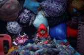 A boy wrapped in a quilt sits on a cot at a parking area on a cold winter morning in the old quarters of Delhi