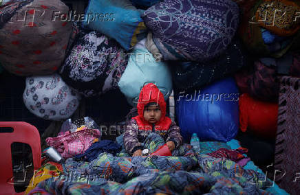 A boy wrapped in a quilt sits on a cot at a parking area on a cold winter morning in the old quarters of Delhi