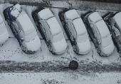 A worker cleans a street where cars are covered in snow amid the first snowfall in Kyiv