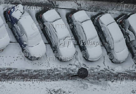 A worker cleans a street where cars are covered in snow amid the first snowfall in Kyiv