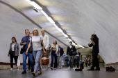 A man plays the violin as people walk in a subway station during morning rush hour in central Kyiv