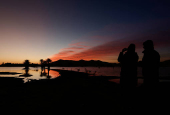 People take photos of sand dunes and palm trees partially covered by floodwaters, after rare rainfall hit the area last September, at dawn in Merzouga