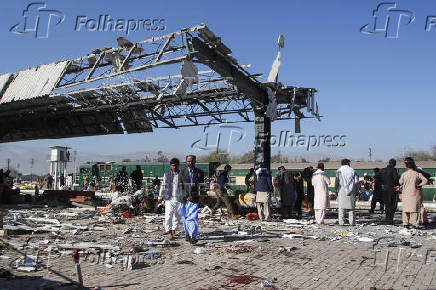 People walk amid debris after a bomb blast at a railway station in Quetta