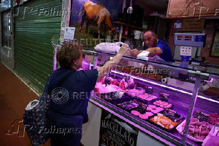 A woman shops pork meat at a market stall in Rome