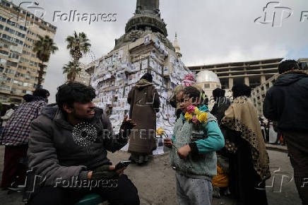 Girl sells flowers near pictures of missing people, in Damascus