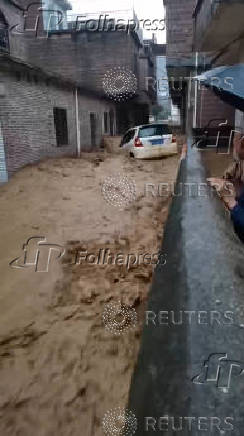 A man looks at a car being swept by fast-moving floodwaters, in Fuyuan village, Guangdong