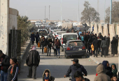 Displaced people who fled Aleppo countryside walk past cars in Tabqa