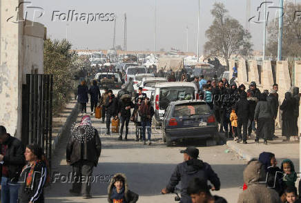 Displaced people who fled Aleppo countryside walk past cars in Tabqa