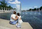 Mother and daughter dip their feet in the cool water at the World War II Memorial in Washington