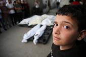 A Palestinian boy stands next to the bodies of Palestinians killed in Israeli strikes, in Rafah
