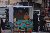 A boy stands on  the back of a vehicle, driving along the market street, in Douma