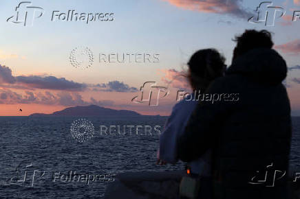 Ischia island is seen as two people hug at sunset on Capri island