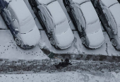 A worker cleans a street where cars are covered in snow amid the first snowfall in Kyiv