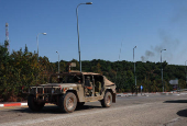 An Israeli military vehicle drives as smoke rises in the background, near Sasa