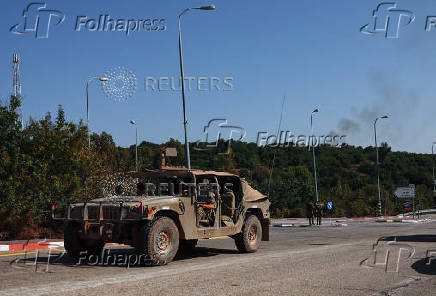 An Israeli military vehicle drives as smoke rises in the background, near Sasa