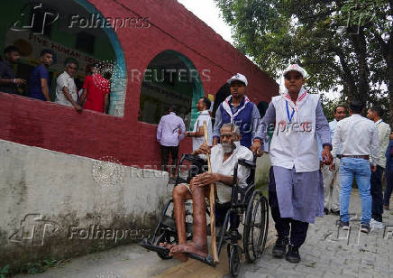 Volunteers assist a man in a wheelchair as he arrives at a polling station to cast his vote during the state assembly elections, in Karnal