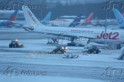 Staff use tractors to help clear snow from around aircraft after overnight snowfall caused the temporary closure of Manchester Airport in Manchester