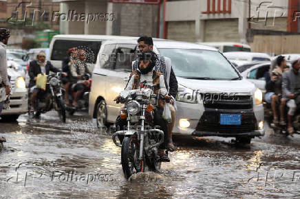 People ride a motorcycle on a flooded street during rains in Sanaa